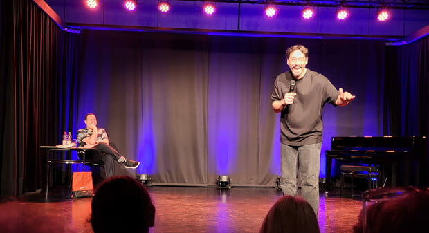 Dichterwettstreit deluxe: Poetry Slam am 25.10.24 im Rahmen der HerbstLese 2024. Sitzend links Moderator Elias Raatz, rechts stehend Special Guest und Comdedian Serkan Ates-Stein.