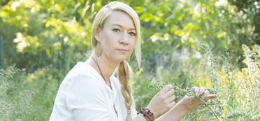 Eine blonde Frau sitzt mit einer Wildblume in der Hand mitten in einer Wiese (Foto: K. Himmelreich-Rades)