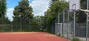 Allwetterbolzplatz an der Kaywaldschule mit rotem Belag und Basketballkorb