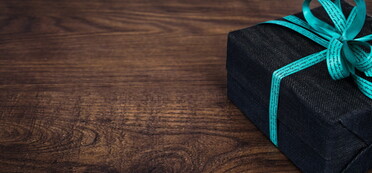 Geschenk mit türkisfarbener Schleife vor dunklem Holzhintergrund (Foto: Harry Strauss/pixabay)