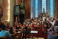	Chor singt in einer Kirche. Menschen sitzen und stehen w&auml;hrend der Auff&uuml;hrung zuh&ouml;rend da. Hier zu sehen: Chor der Regiswindiskirche, Vokalensemble Novere - Aufnahme aus dem Konzert "H&ouml;rst Du nicht die B&auml;ume rauschen?" vom 19.7.2026 unter der Leitung von Katharina Linn (stehend links); Texte und Lesung: Dorothee Kr&auml;hmer (2.v.l., stehend)