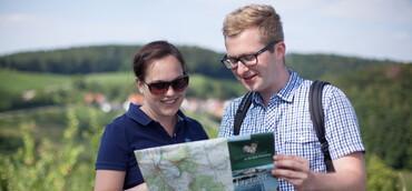 Ein Mann und eine Frau betrachten eine Wanderkarte; im Hintergrund Weinberge (Foto: TG Heilbronner Land)