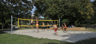 Junge Männer spielen auf dem Beachvolleyballfeld am Kiesplatz