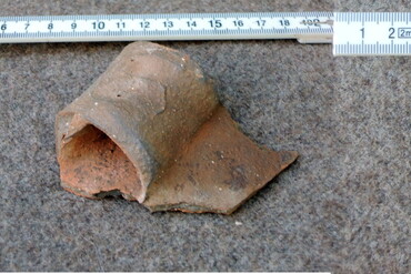Archäologisches Fundstück aus Ton liegt neben einem Meterstab 
